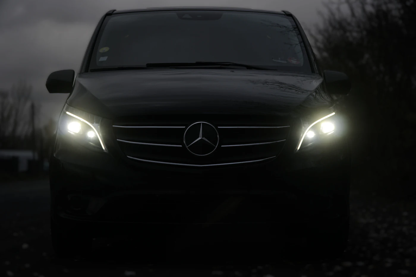 A black Mercedes-Benz V-Class at dusk, headlights on